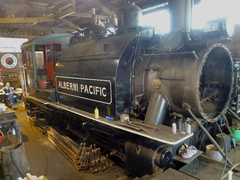 The Number 7, in the shop for repairs with the saddle water tank still installed, is owned by the City of Port Alberni and is cared for by the Western Vancouver Island Industrial Heritage Society. The shell was stripped bare to the water tank and the tubes & tube sheets for inspection. Laying on the floor next to #7 you can see the superheaters that were removed from the flue tubes that were later installed back into the boiler. 